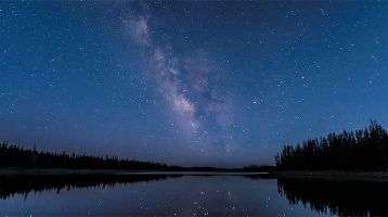 Starry night sky above a tree-lined river