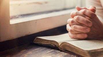 Hands clasped in prayer on a bible.